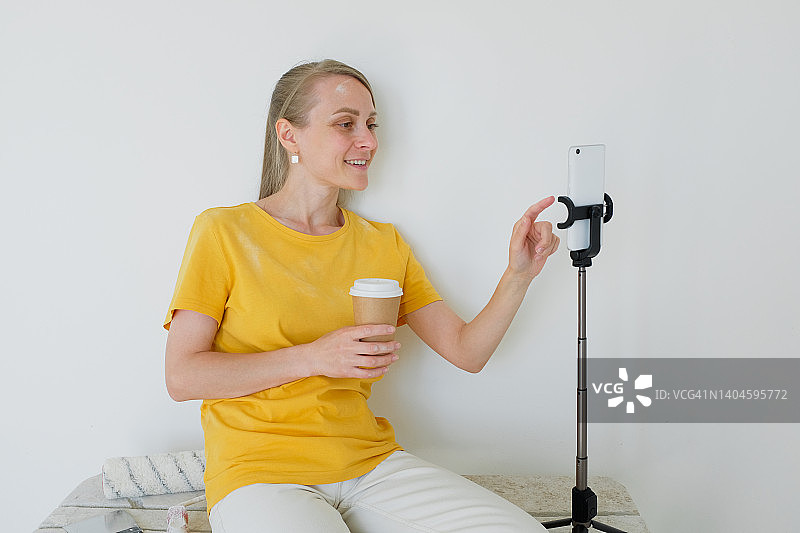 建筑女博主在镜头前广播或展示，喝着咖啡。 建筑工具在附近。 专业维修和施工的概念，爱好。 视频通话，视频会议，虚拟活动。图片素材