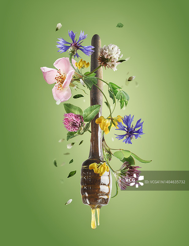 飞舞的木制蜂蜜勺，滴着蜂蜜和色彩鲜艳的野花，绿色背景图片素材