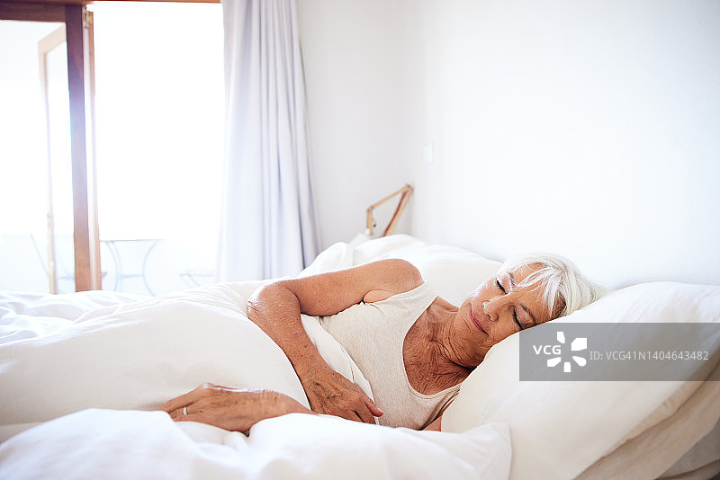 阳光明媚的早晨，一位年长的女人在床上睡觉图片素材