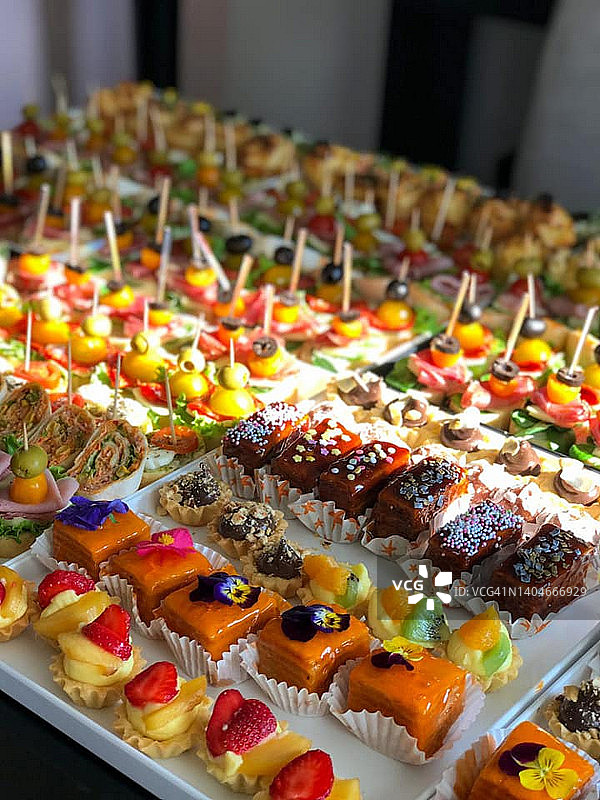 在一家大型餐厅里，宴会桌上摆满了美味的甜饼干、纸杯蛋糕和松饼。图片素材