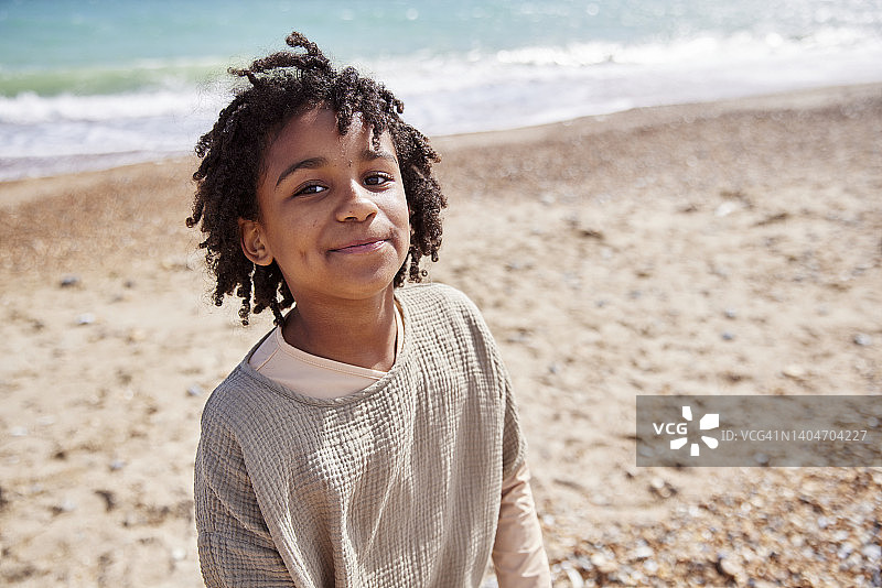 年轻帅气的7岁男孩对着镜头微笑，在海滩享受家庭日。图片素材