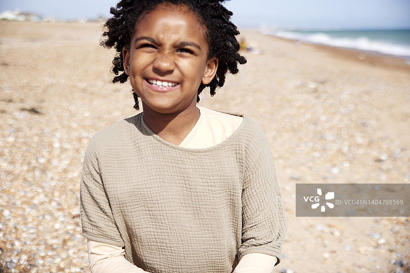 7岁的年轻男孩看着镜头，在海滩上享受家庭日图片素材