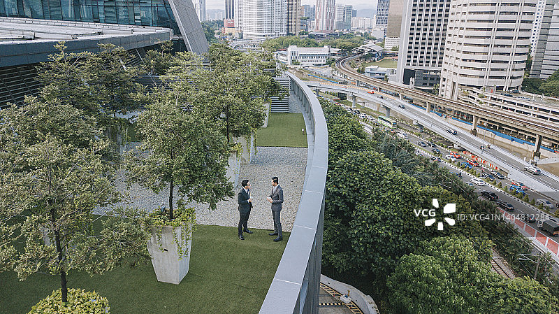 两名商人于办公楼外屋顶花园交谈（俯视）图片素材