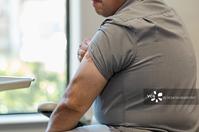 一位接种流感疫苗后手臂上贴着绷带的男士图片素材