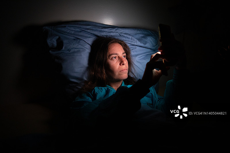 女人躺在床上使用手机图片素材