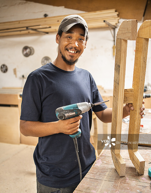 在车间使用钻头组装椅子的微笑工人图片素材
