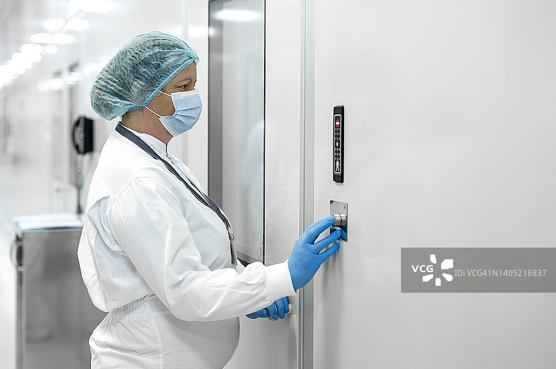 在制药实验室的女职员穿着防护设备，通过按钮开门图片素材