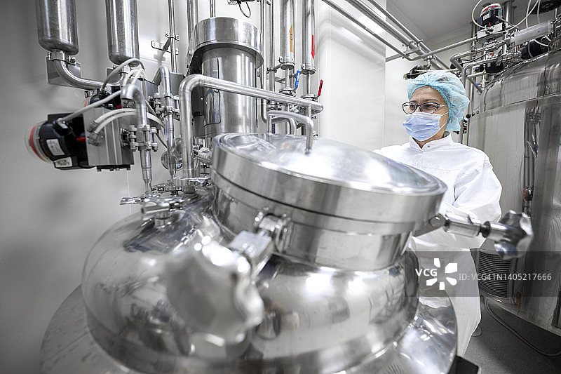 戴着眼镜，全副武装穿着防护工作服的女人在制药制造期间在实验室工作图片素材