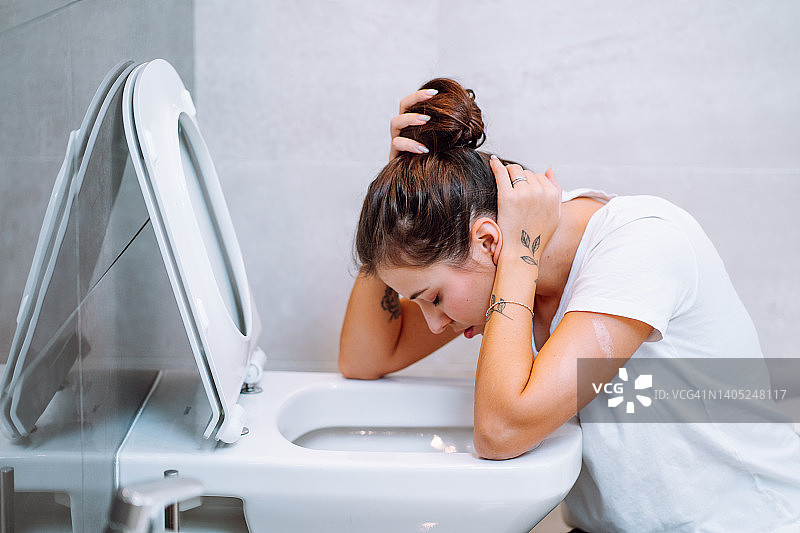 年轻女人感到恶心，坐在马桶旁呕吐，妊娠中毒图片素材