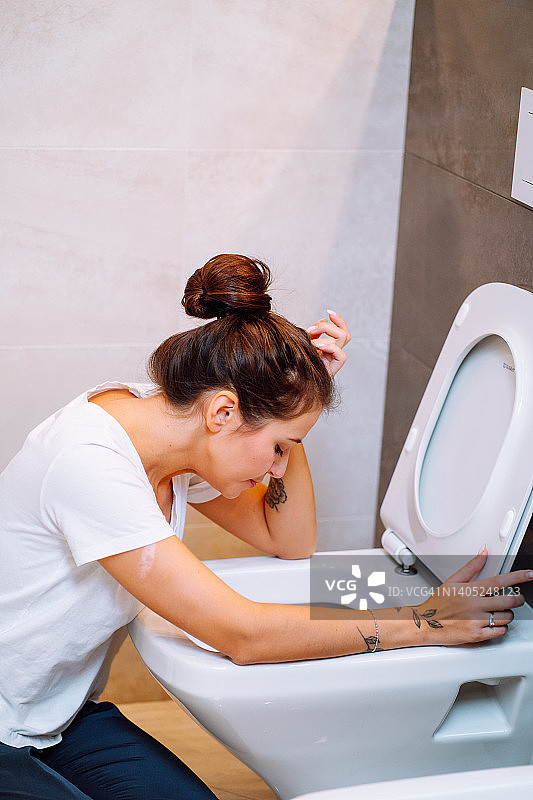 年轻女子感到恶心，坐在马桶旁呕吐图片素材