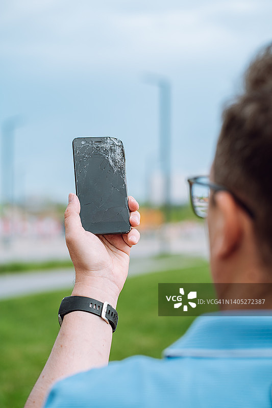男子手持黑色破损智能手机，检查其工作状态图片素材
