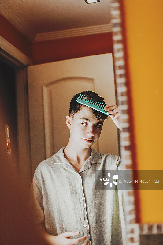 年轻男子在浴室梳头，看着镜子里的自己图片素材