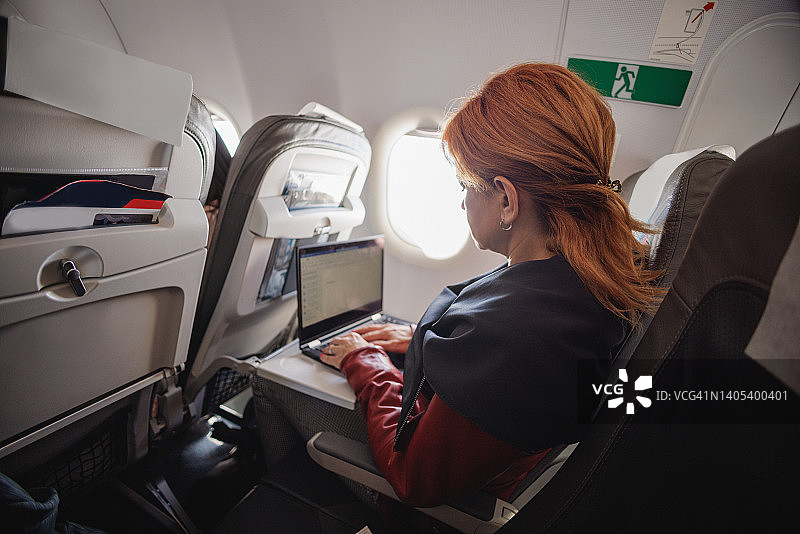 女人在飞机靠窗座位上使用笔记本电脑图片素材