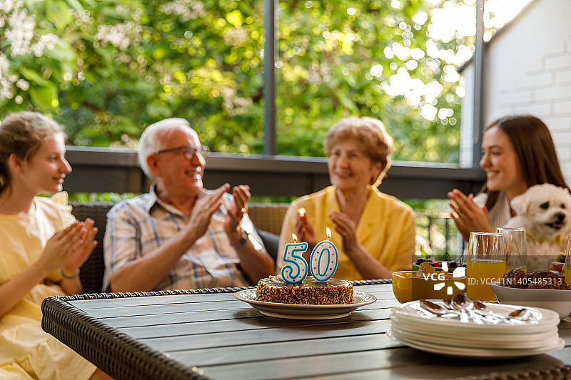 蛋糕上的燃烧的蜡烛，老年夫妇和孙女们鼓掌图片素材