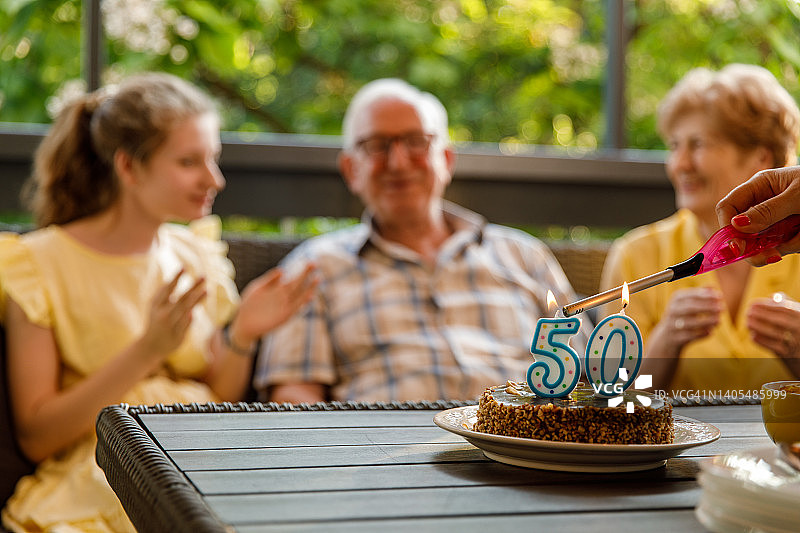 一位女士为年长的父母点燃周年纪念蛋糕上的蜡烛图片素材