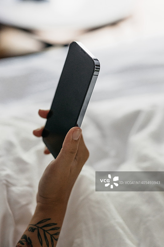 在床上拿着iPhone的有纹身女人图片素材