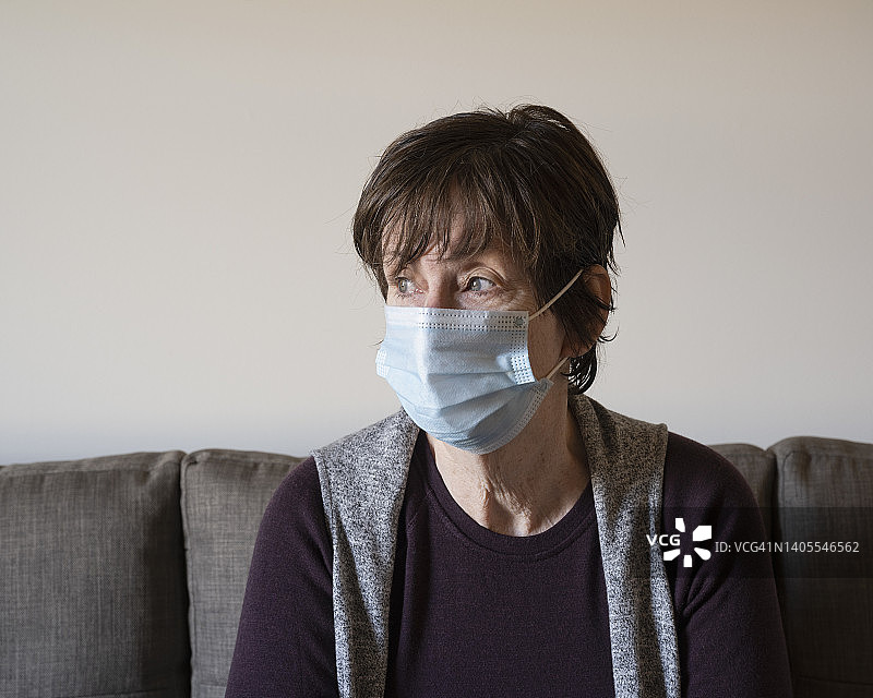 戴着口罩坐在沙发上的焦虑的女人图片素材