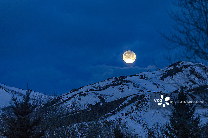 美国爱达荷州贝尔维尤夜晚白雪覆盖的山丘上的满月图片素材