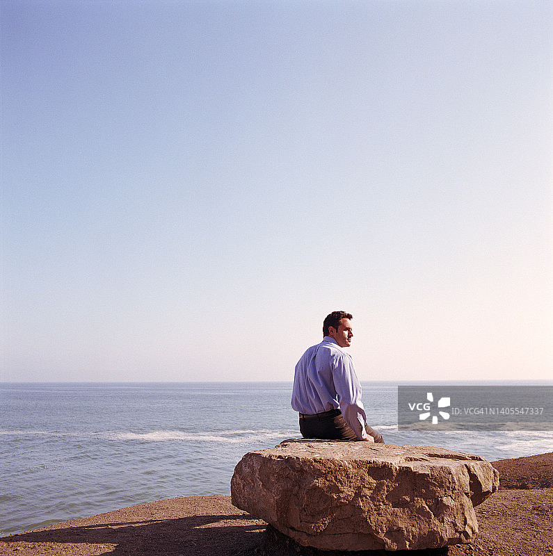 美国加利福尼亚州穆古角海滩上坐在岩石上的商人图片素材