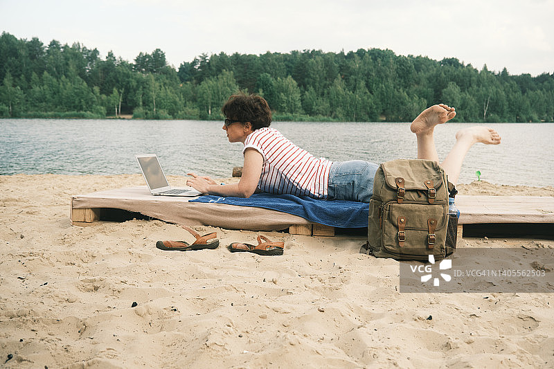 女人在森林湖岸边休息时使用笔记本电脑工作图片素材