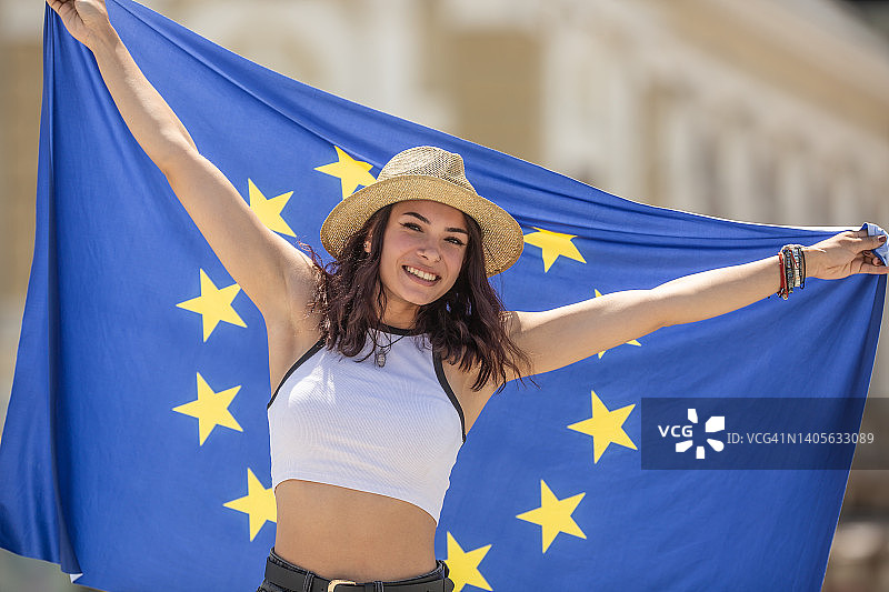 快乐的年轻女人在欧洲的街道上挥舞着欧盟旗帜图片素材