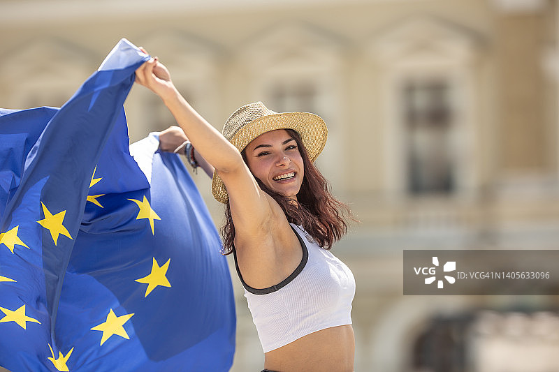 快乐的年轻女人在欧洲的街道上挥舞着欧盟旗帜图片素材