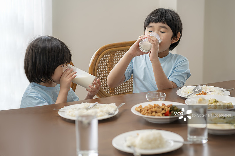 亚裔儿童在餐桌上喝牛奶，反映家庭良好关系图片素材