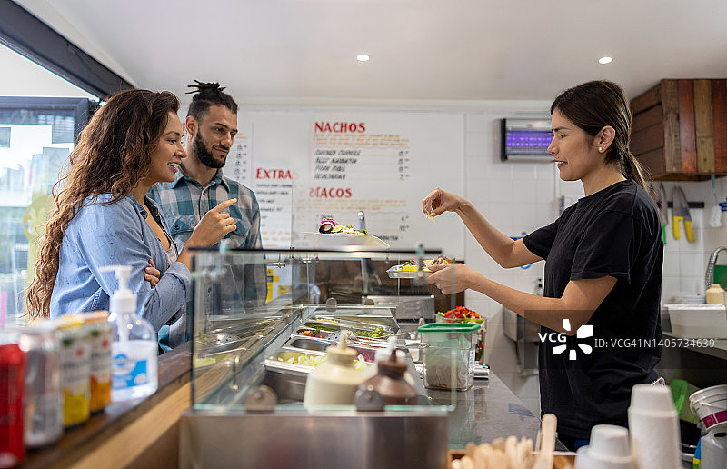 女服务员在街头小吃店为顾客准备墨西哥卷饼图片素材