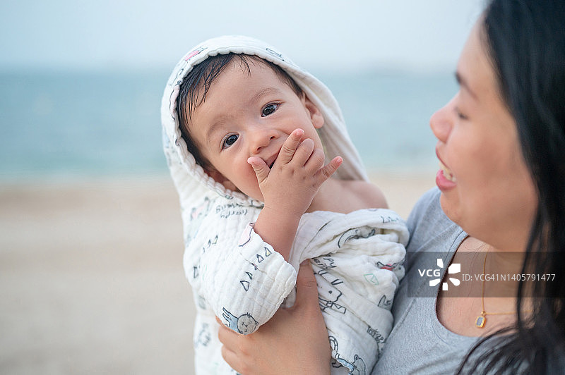游泳后，母亲抱着裹着毛巾吃饼干的宝宝图片素材