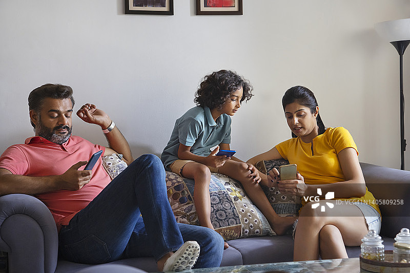 在客厅里使用智能手机的快乐家庭图片素材