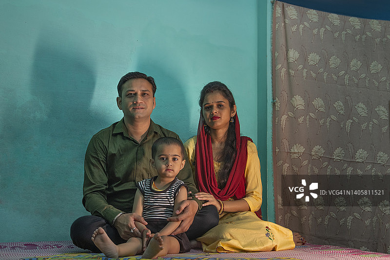 快乐的父母和孩子坐在床上看着镜头的肖像图片素材