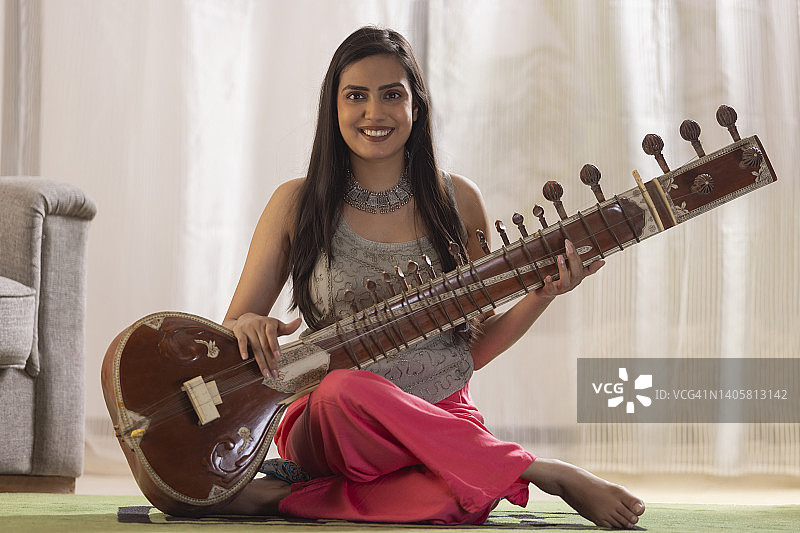 快乐的年轻女音乐家在家弹奏西塔琴的肖像图片素材