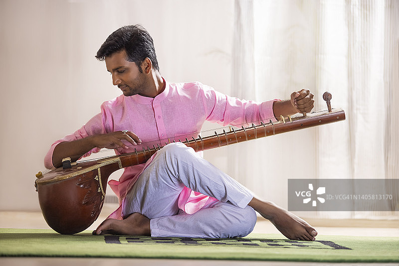 年轻男音乐家在客厅里弹奏西塔琴图片素材