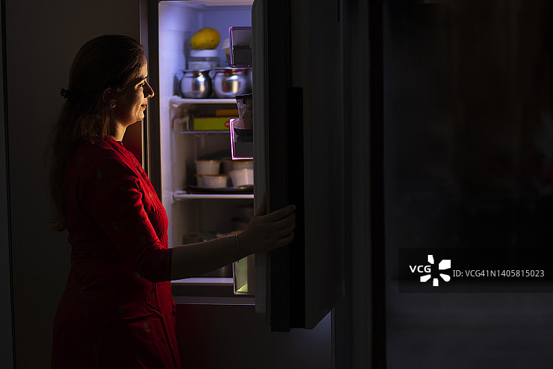 年轻女子在厨房里查看冰箱内部图片素材