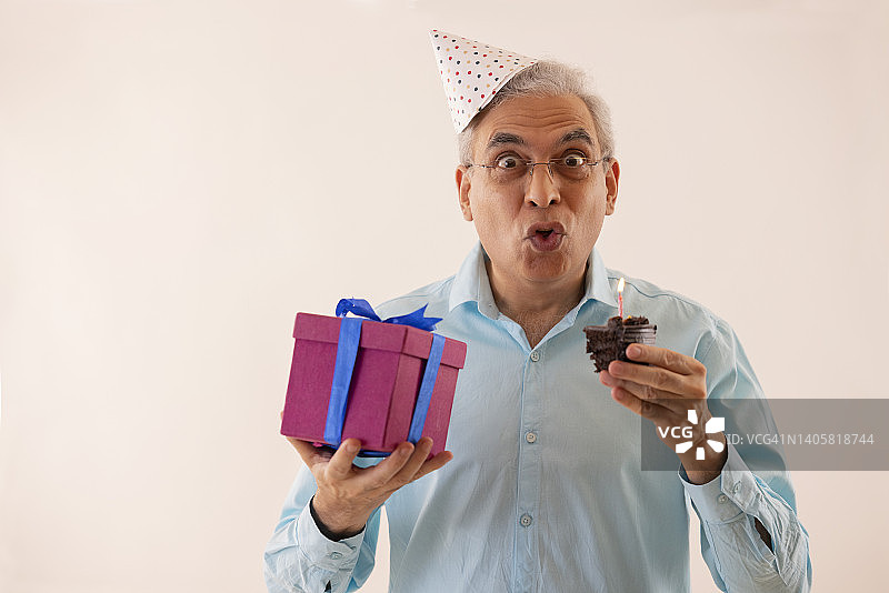 手捧生日蛋糕和礼物的惊讶老年男人肖像图片素材