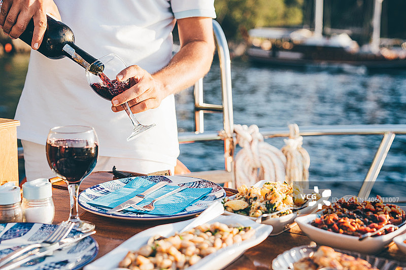 朋友在游艇上喝葡萄酒，欣赏日落。男人在倒酒图片素材