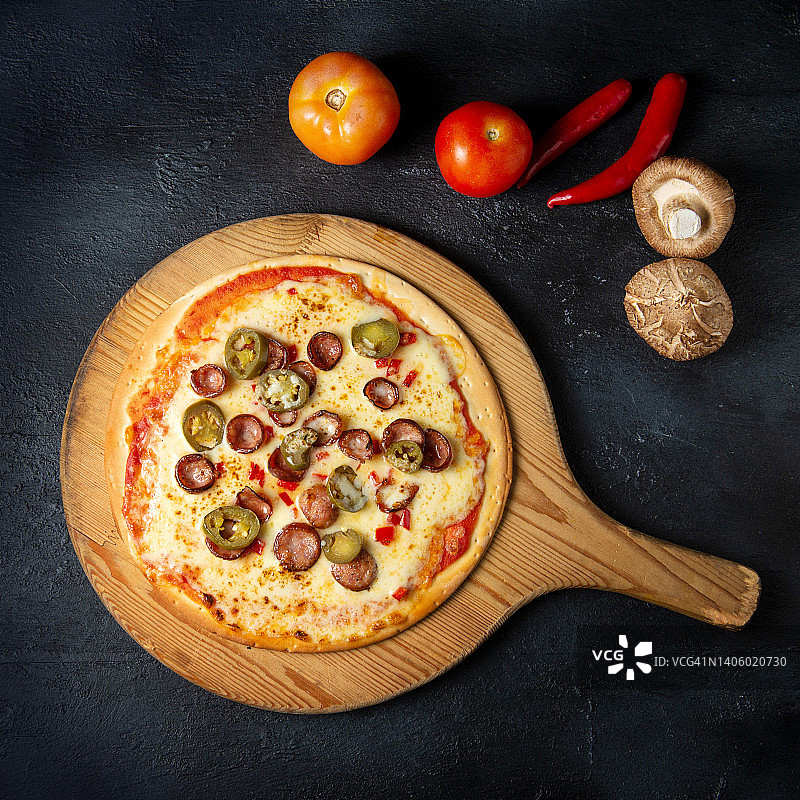 美味披萨配香肠和青辣椒，木盘，深色背景图片素材