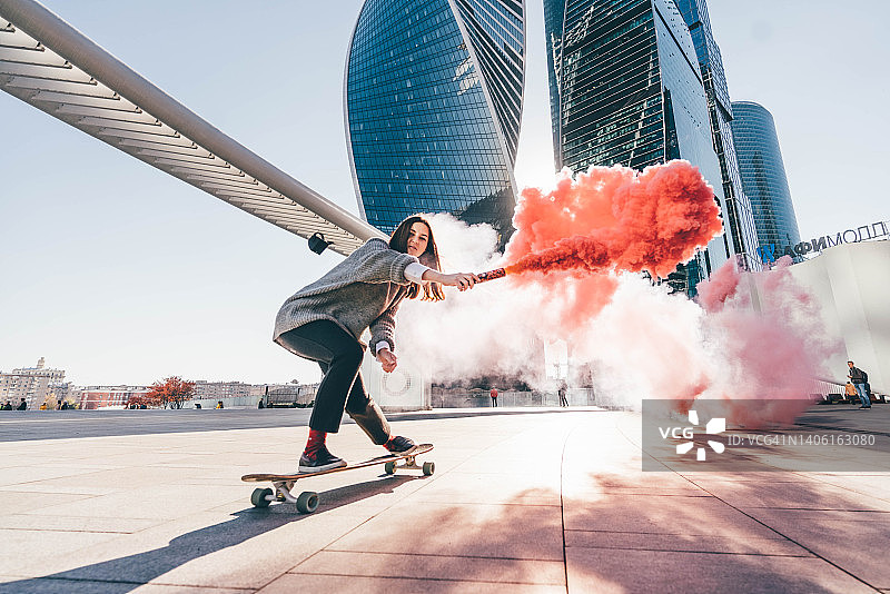 年轻女子在城市里玩彩色烟雾滑板图片素材