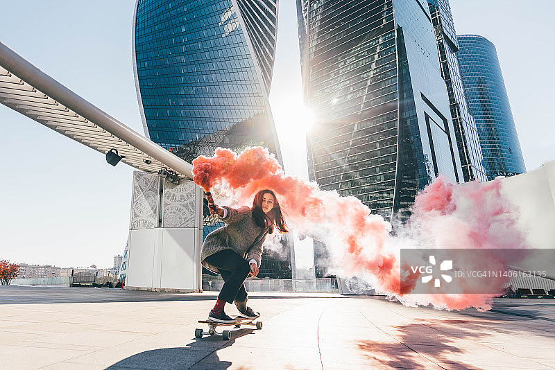 年轻女子在城市里玩彩色烟雾滑板图片素材