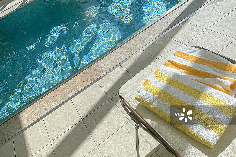 酒店室内游泳池和明亮阳光下躺椅上条纹黄色毛巾特写图片素材
