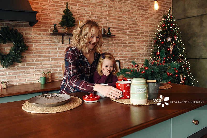 金发母亲和女儿站在厨房里。圣诞厨房装饰。母女俩在喝茶。圣诞氛围。母女间的互动图片素材
