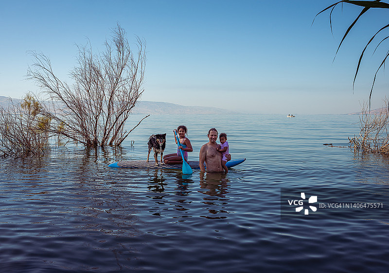 活跃的家庭和水上运动。父亲、混血姐妹和狗在夏季度假时一起玩桨板。图片素材