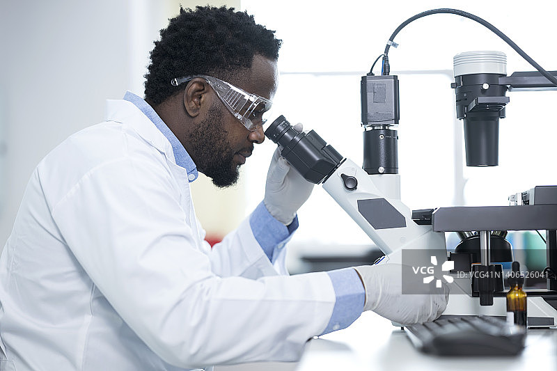 人类遗传学和基因组医学研究。非裔美国人实验室技术员在医学实验室研究基因组样本时，通过显微镜观察的侧视图图片素材