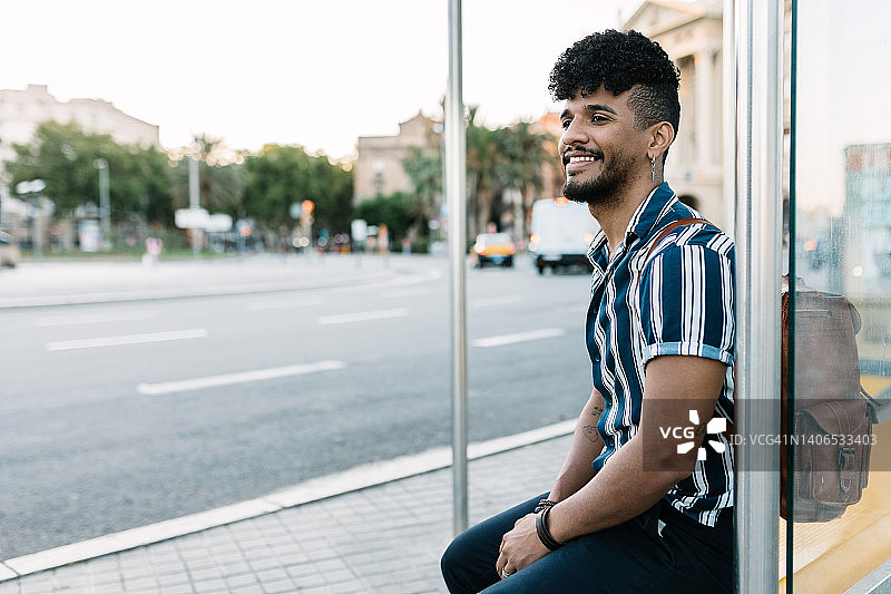 在城市车站等候城市公交车的年轻西班牙裔拉丁男人。图片素材
