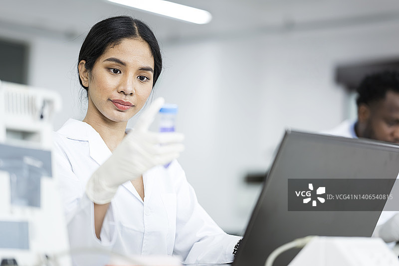 医学研究的实验结果程序操作研究员在检查化学品时拿着试管并将检测结果记录到医疗实验室的笔记本电脑中图片素材