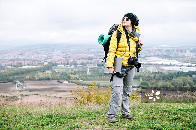 背着登山包、脖子上挂着相机、右手拿着笔记本电脑的数字游民女性图片素材