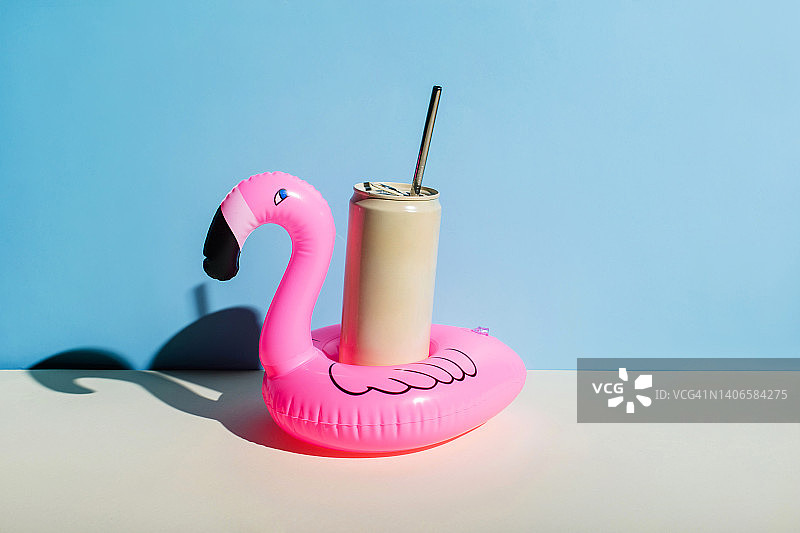 蓝色背景下手拿冰镇饮料的粉色充气火烈鸟图片素材