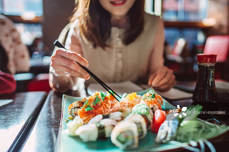 年轻女人享用新鲜制作的寿司拼盘图片素材