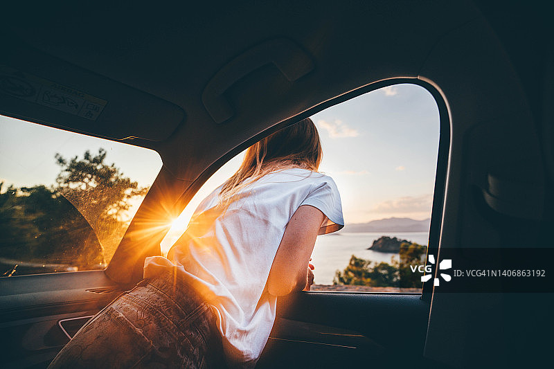 年轻女子在日落时分享受兜风乐趣，可爱年轻女子挂在车窗外图片素材
