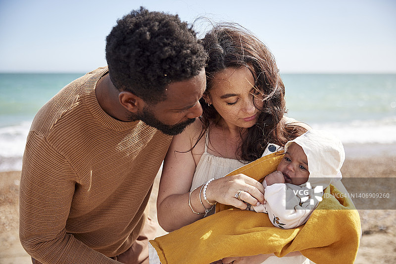 父母爱怜地看着刚出生的女儿，在海滩上享受她的第一次旅行图片素材